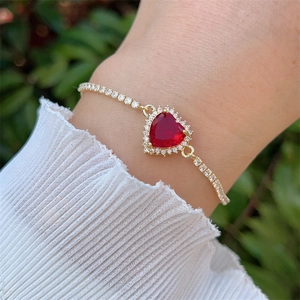 Detail of a 18K gold plated heart bracelet with red zircon worn on a woman's wrist
