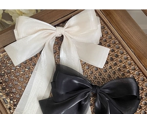 Macro detail of oversized satin ribbon bow hair clips in cream white and black finishes