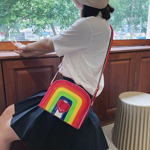 Detail of a shiny patent leather rainbow crossbody bag featuring a central red heart patch