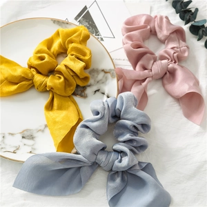 Set of three satin bow hair scrunchies in yellow, pink, and light blue on marble tray
