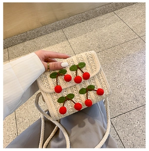 Close-up of white woven straw crossbody bag with handmade red cherry decor