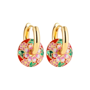 Nahaufnahme von goldenen Creolen mit roten Emaille-Anhängern und rosa Kirschblütenmustern