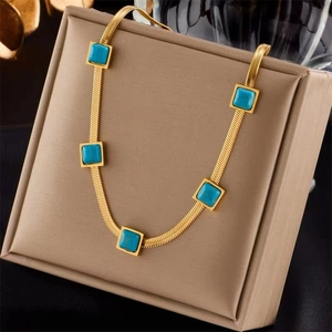 Golden snake chain necklace with five square turquoise stones on a beige jewelry box