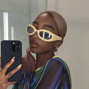 Close-up of beige oval Y2K sunglasses with wide arms worn in a casual indoor setting