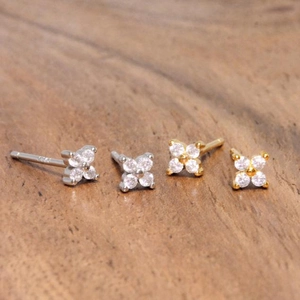 Macro shot of silver and gold S925 four-petal flower stud earrings on wood surface