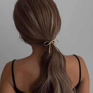 Elegant gold metal bow hair tie accessory on low ponytail for women's hairstyle