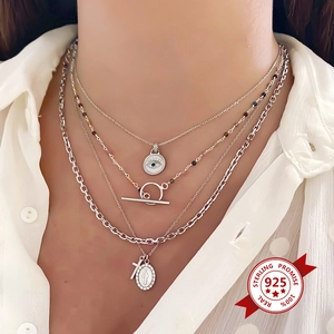 Close-up of layered S925 silver necklaces with evil eye coin and Mary cross charms
