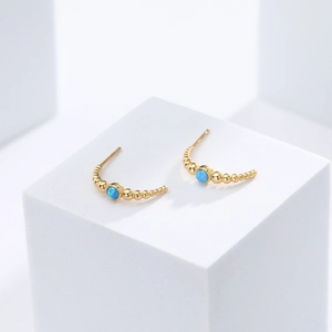 Close-up of golden S925 silver stud earrings with blue opal stones and minimalist design