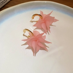 Close-up of matte pink acrylic petal earrings with golden C-shape hooks in a ceramic dish