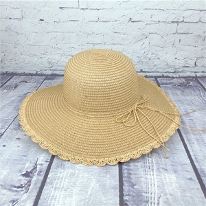 Detail view of the scalloped wavy edge and bow tie on a khaki straw sun hat