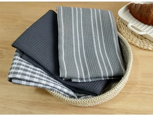 Close-up of waffle weave cotton tea towels in grey and stripes folded in a wicker basket
