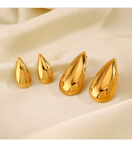 Macro detail of polished 18K gold teardrop earrings on elegant beige silk fabric