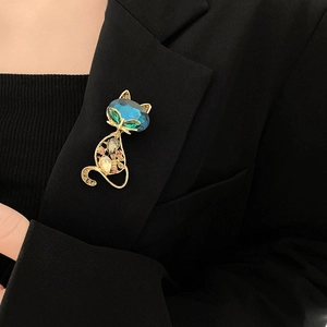 Detailed close-up of a golden cat brooch with blue and green crystals on a black suit