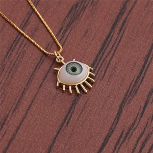 Detailed close-up of a gold-plated evil eye necklace with green pupil on textured background