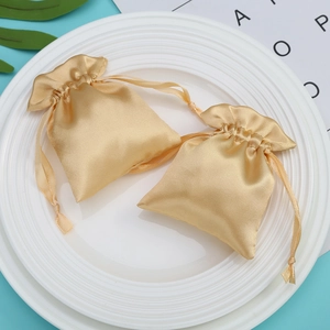 Champagne satin drawstring bag for jewelry storage shown on white ceramic plate