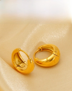 Detailed view of chunky gold-plated C-shape hoop earrings on champagne satin fabric