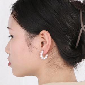 Close-up of elegant C-shaped pearl hoop earrings worn by a model in soft lighting