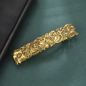 Detail of vintage golden hair clip with embossed sunflower and leaf scroll patterns