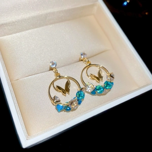 Detail of gold butterfly drop earrings with blue gradient crystals on a silk lining