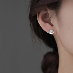 Macro shot of a model wearing a seashell-shaped silver earring with blue enamel finish