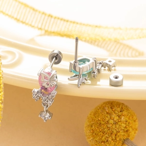 Silver butterfly earrings with pink and teal stones and screw back on a warm background