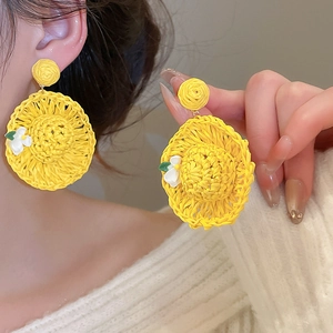 Close-up of handmade yellow raffia straw hat earrings with white flower detail