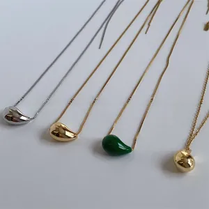 Detailed view of teardrop pendants in gold, silver, and green on various sleek chains