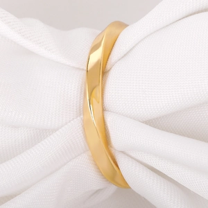 Macro shot of minimalist gold Mobius ring with mirror finish on white textured fabric