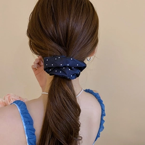 Detailed view of a dark blue polka dot satin scrunchie on a low ponytail hairstyle