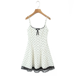 Detailed view of white polka dot dress with black bow and lace hem on wooden hanger