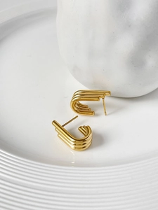 Detailed view of layered U-shaped 18K gold earrings on a minimalist ceramic dish