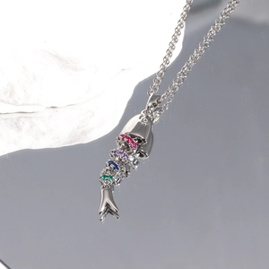 Macro detail of silver articulated fish pendant with colorful gems on reflective surface