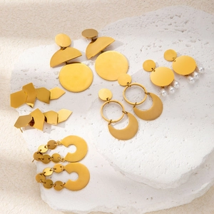 Detailed view of gold geometric earrings with pearls on white stone surface