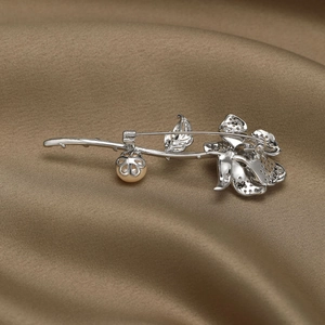 Détails d'une broche rose avec pétales argentés, texture de feuille et perle