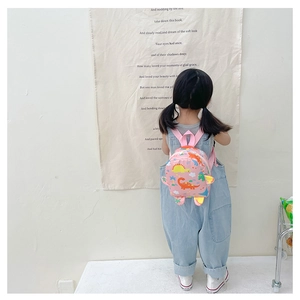 Toddler wearing pink cartoon dinosaur backpack featuring bright yellow horns and cute patterns