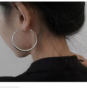 Close-up of minimalist large silver hoop earrings with thick gradient tubing on a model