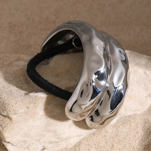 Detail of silver liquid metal wave hair tie on white rock under natural sunlight