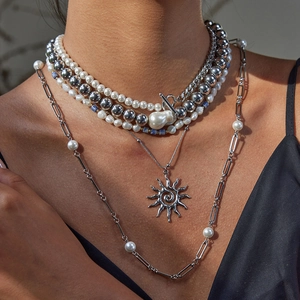 Detail view of layered silver necklace set with pearls and a sun pendant on model