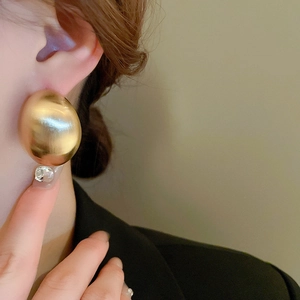 Detail of matte gold geometric oval stud earring on model showing brushed metal texture
