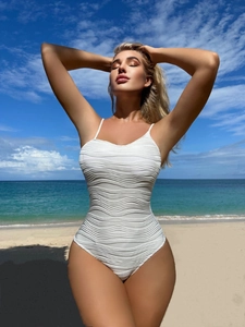 Detail of white one-piece swimsuit featuring unique wavy texture on beach background