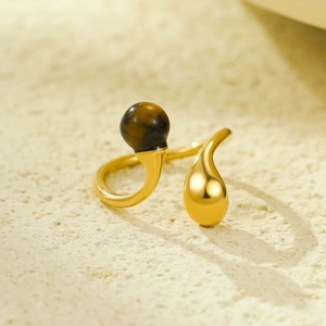 Vue macro d'une bague dorée en acier inoxydable avec pierre oeil de tigre sur sable