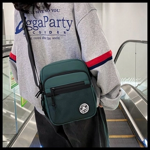 Dark green nylon messenger bag with multi-layer zipper shown on an escalator