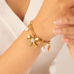 Gold plated bow bracelet with white imitation pearls and star pendants on woman wrist