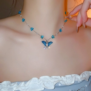 Primer plano de un collar con colgante de mariposa azul y perlas en el cuello