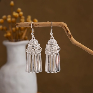 Detailed view of silver ethnic tassel earrings with metal pillars hanging on a branch