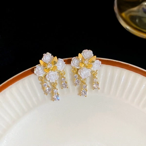 Macro view of floral stud earrings with butterfly charms and zircon tassels on dark background