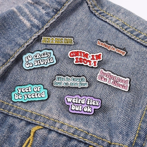 Close-up of colorful enamel letter pins with motivational quotes on denim jacket