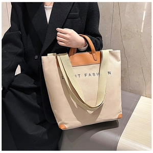 Close-up of beige canvas tote bag with brown leather handles and adjustable shoulder strap