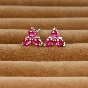 Macro view of clover-shaped stud earrings with pink gemstones on brown velvet