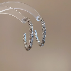 Detailed close-up of silver twisted rope C-shaped hoop earrings on a display stand
